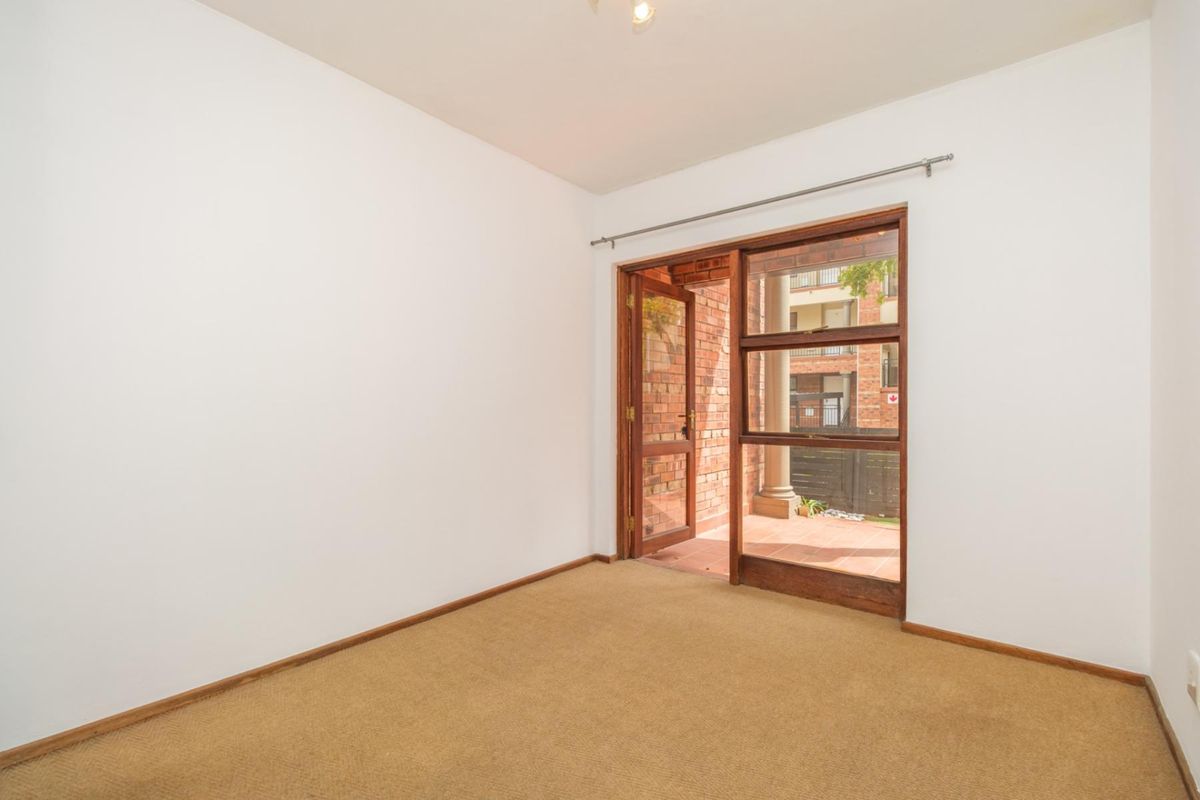 An empty bedroom featuring neutral walls, carpeted flooring, and a timber-framed glass door providing direct access to an outdoor patio area.