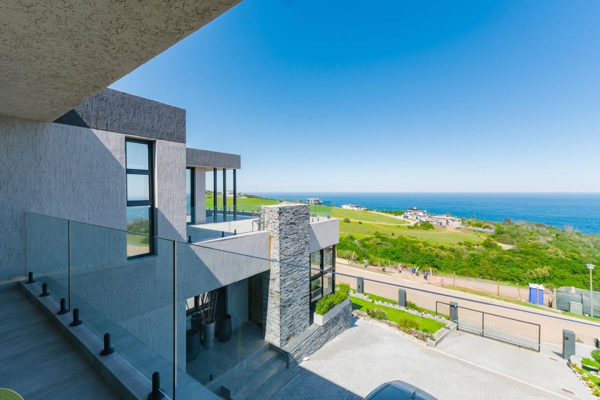 Modern multi-level architectural home featuring stone cladding, glass balustrades, and expansive ocean views from the upper balcony.