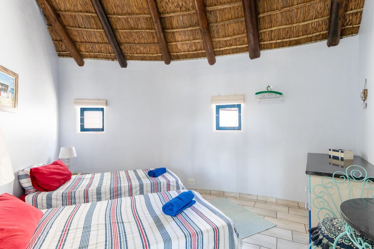 A bedroom featuring a high vaulted thatched ceiling with exposed timber beams, tiled flooring, and two small windows with blue frames.