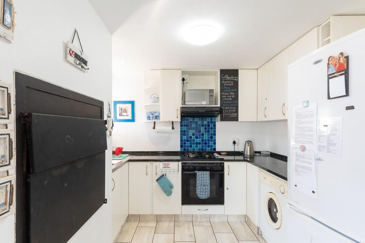 Compact kitchen featuring white cabinetry, dark countertops, a blue tiled backsplash, built-in oven, gas hob, and integrated laundry appliance space.