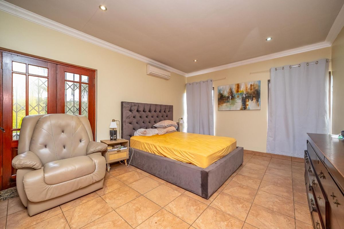 Spacious bedroom featuring tiled flooring, recessed ceiling lighting, a wall-mounted air conditioning unit, and direct access to the exterior via wooden framed glass doors.