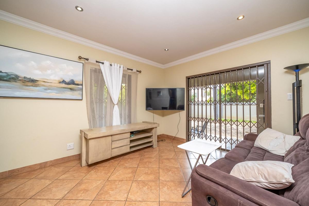 A comfortable living room featuring tiled flooring, recessed ceiling lighting, and sliding glass doors with security gates leading to the outdoor area.