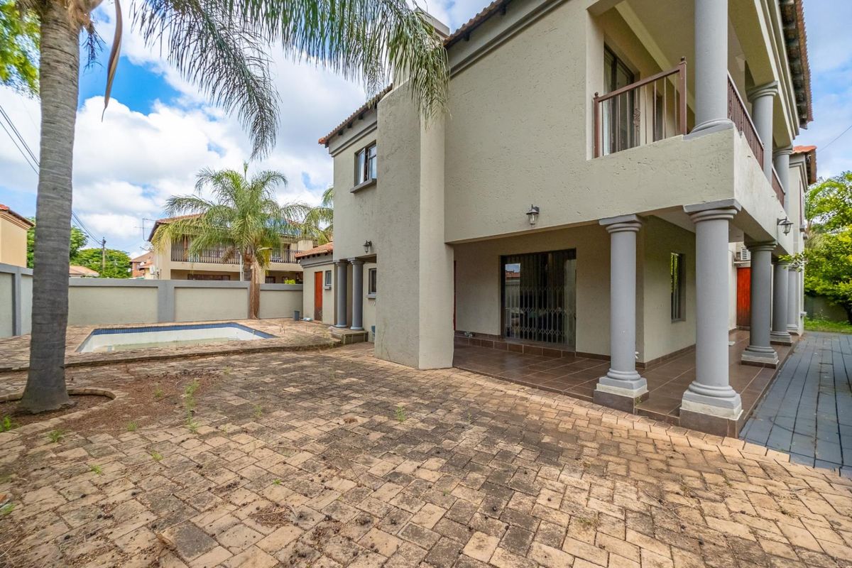 Rear exterior view featuring a covered patio, paved courtyard area, and a swimming pool, showcasing the property's outdoor living space and structural facade.