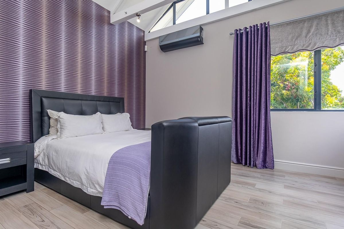 A well-maintained bedroom featuring vaulted ceilings, exposed beams, wood-look flooring, and a wall-mounted air conditioning unit.