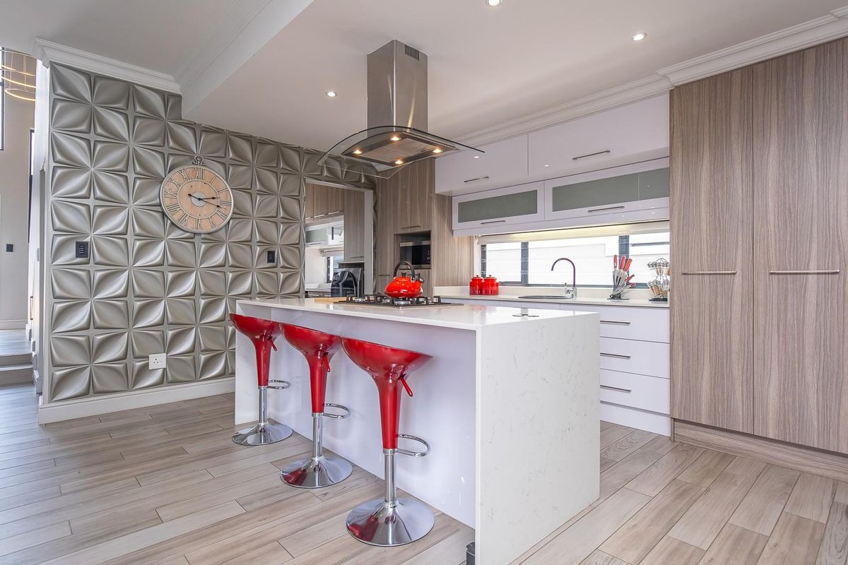 Modern kitchen featuring a central island with a built-in gas hob, stainless steel extractor fan, sleek cabinetry, and a textured feature wall.