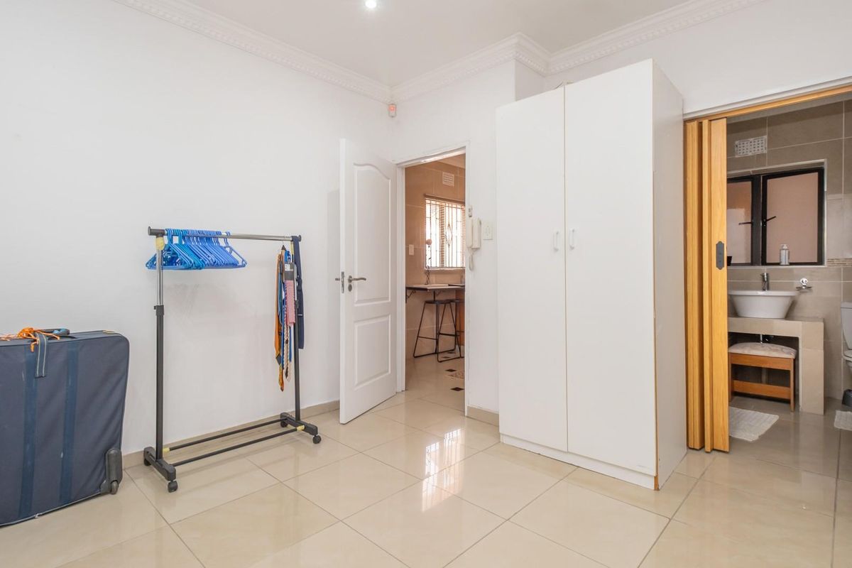 A bedroom featuring tiled flooring, built-in wardrobe, and an en-suite bathroom with a vanity and toilet.