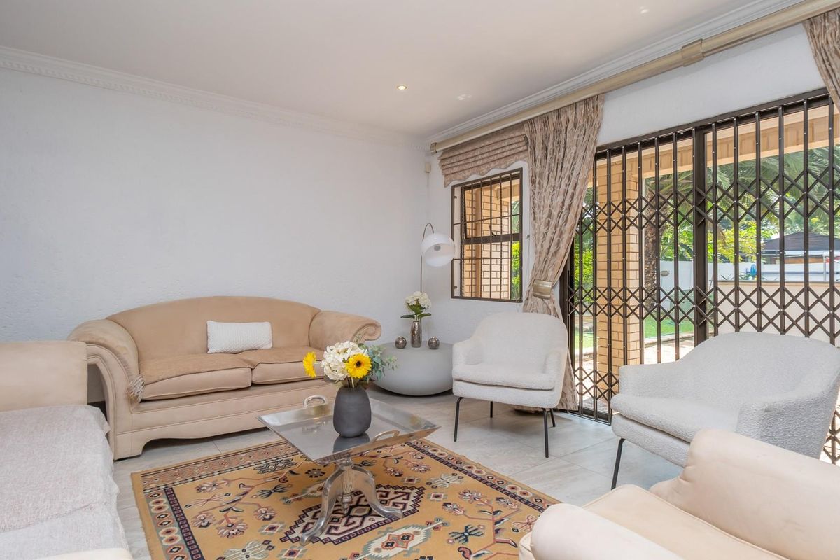 A bright living room featuring tiled flooring, recessed lighting, and large sliding glass doors with security gates leading to an outdoor patio area.