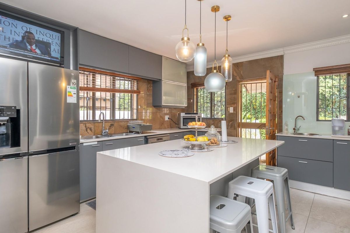 Modern kitchen featuring a central island with stone countertop, grey cabinetry, tiled splashbacks, and integrated sink areas with natural light.