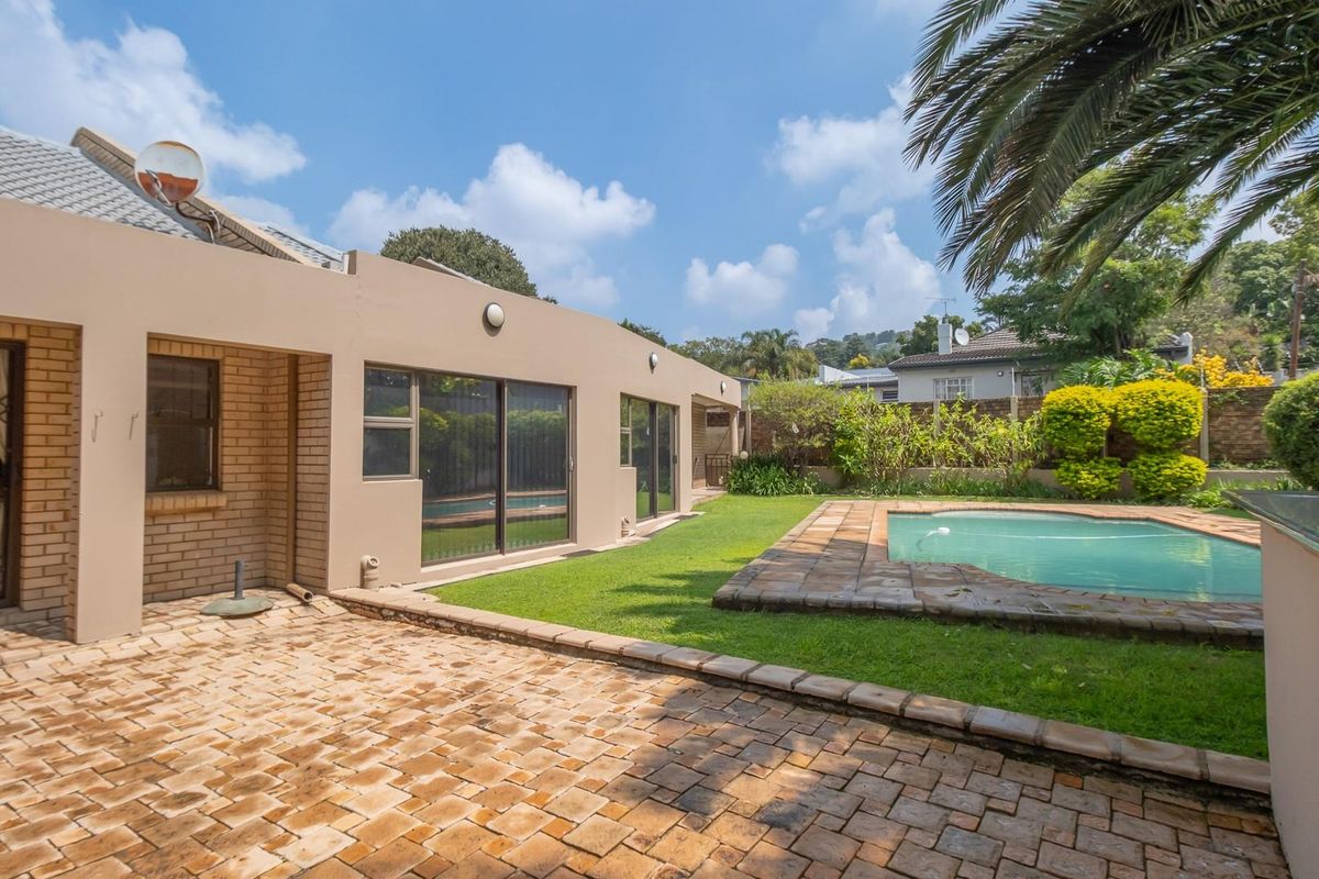 Rear exterior view featuring a paved patio area, a swimming pool, and a landscaped garden with established greenery.