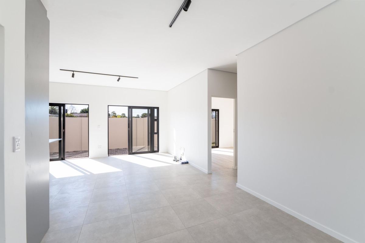 A bright, modern, and spacious open-plan living area featuring neutral tiled flooring, contemporary track lighting, and large aluminium sliding doors leading to the exterior.