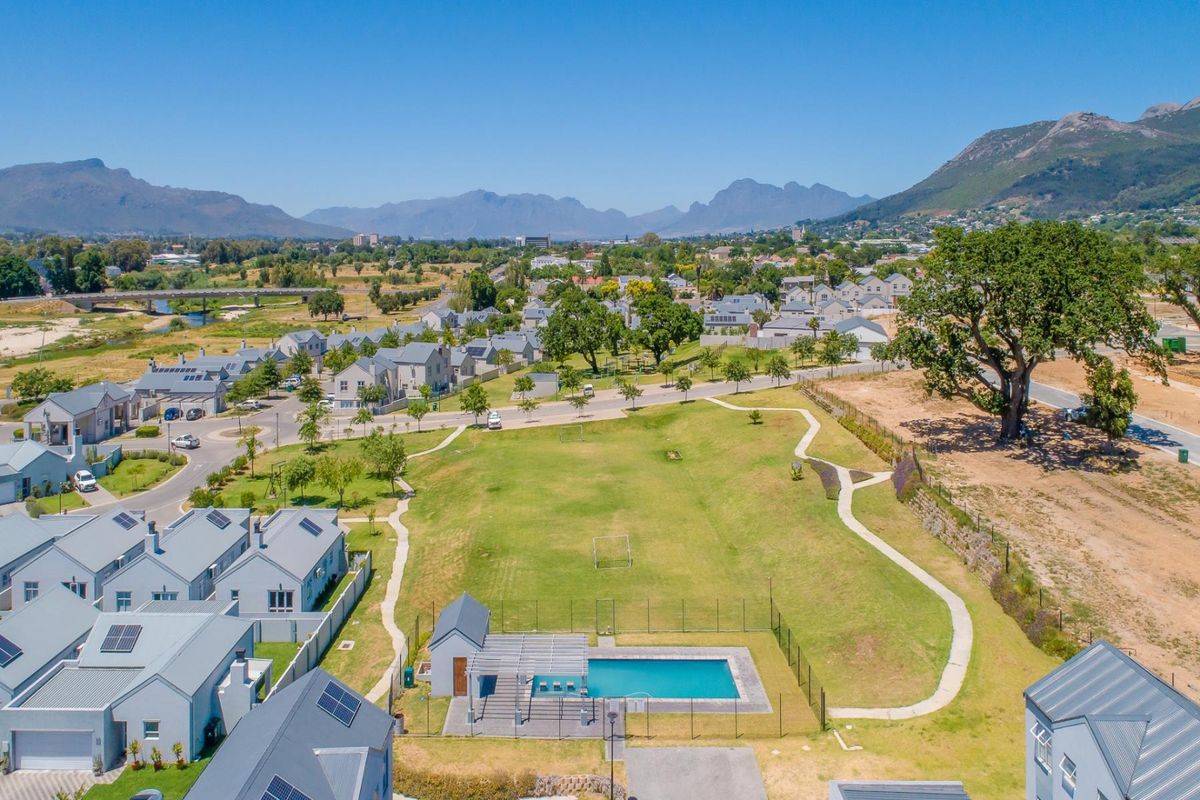 Aerial view of a residential estate featuring a communal swimming pool, landscaped green space, and surrounding mountain views.