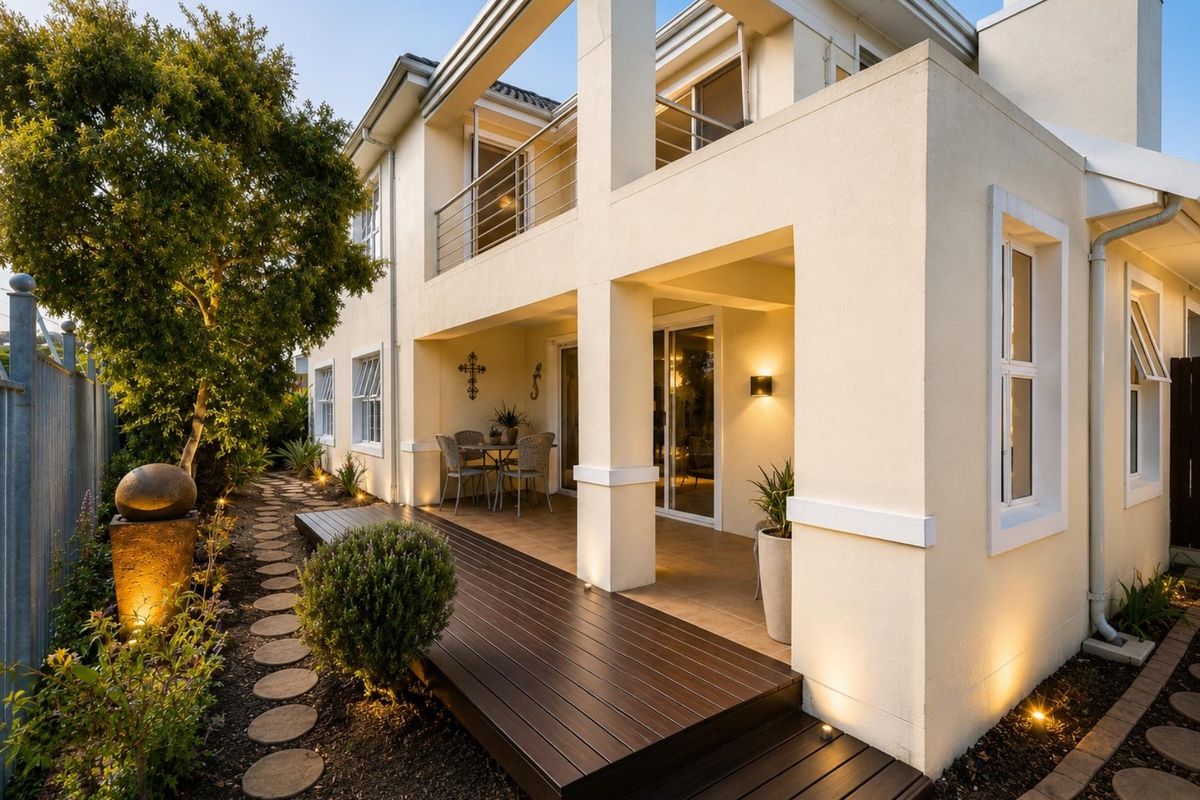 A well-maintained rear exterior featuring a timber deck, tiled patio area, and an upper-level balcony with stainless steel balustrades.