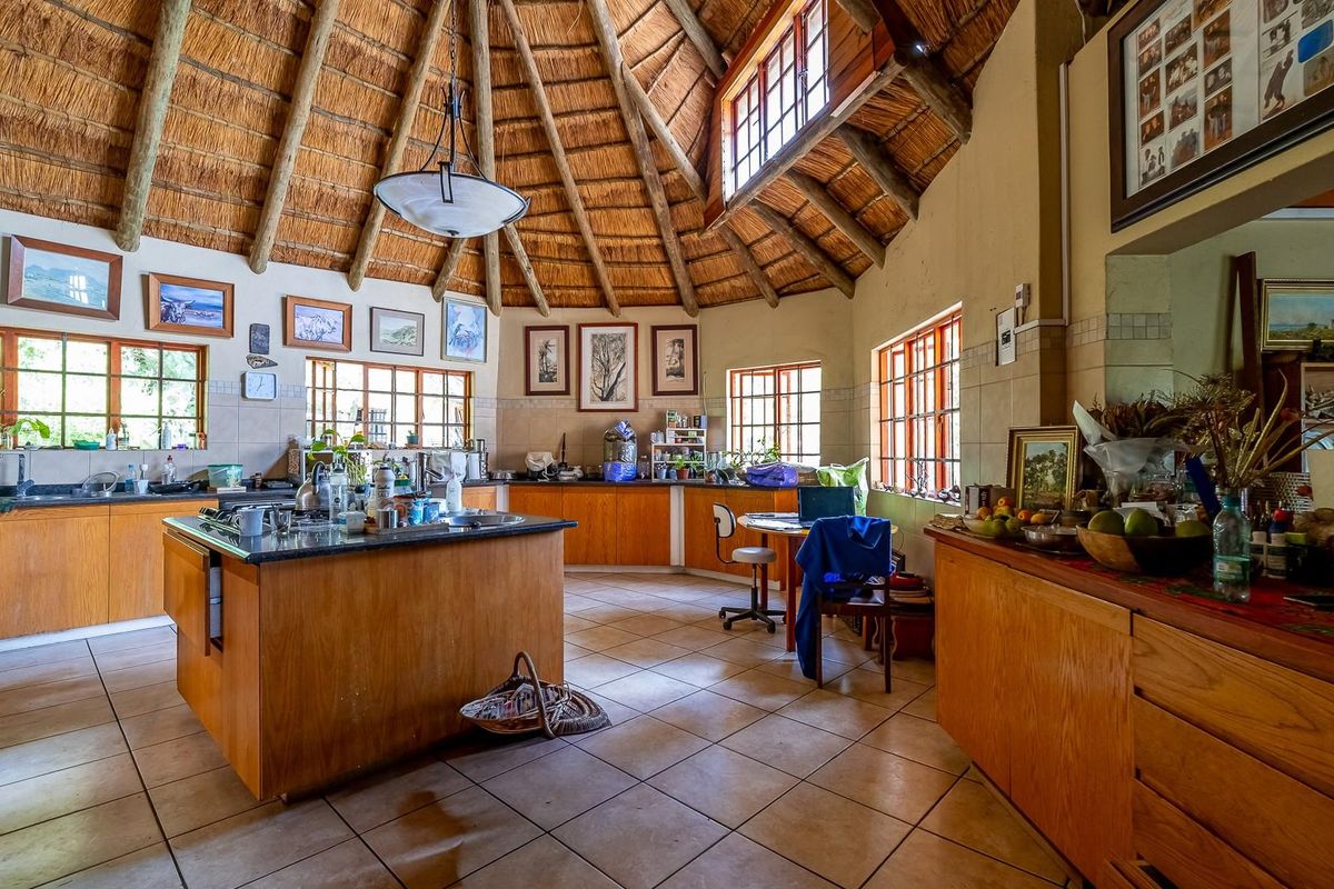Spacious farmhouse kitchen featuring a high thatched roof, central island, wooden cabinetry, and large windows providing ample natural light.