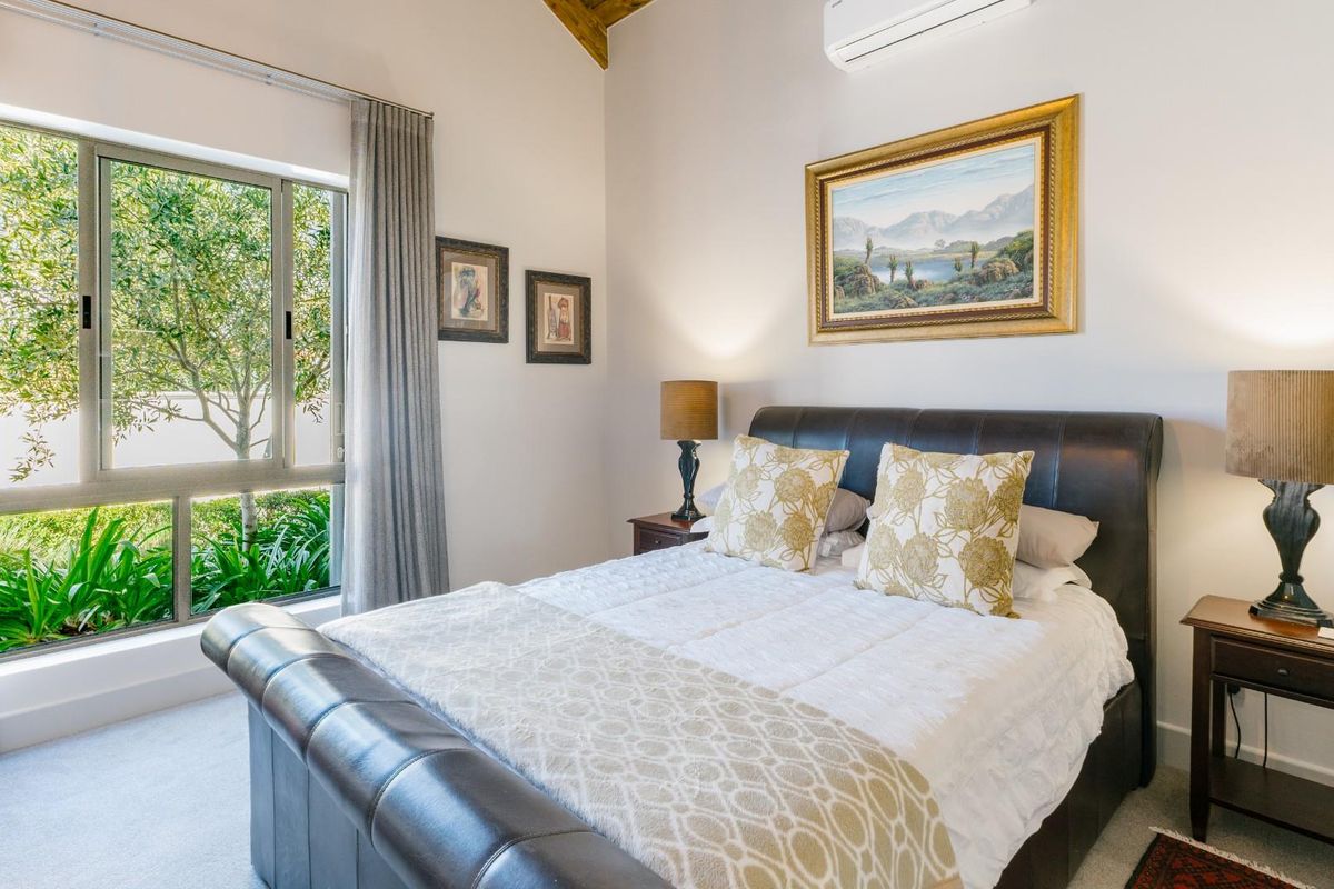 A well-lit bedroom featuring high vaulted ceilings, a large window with garden views, and a wall-mounted air conditioning unit.