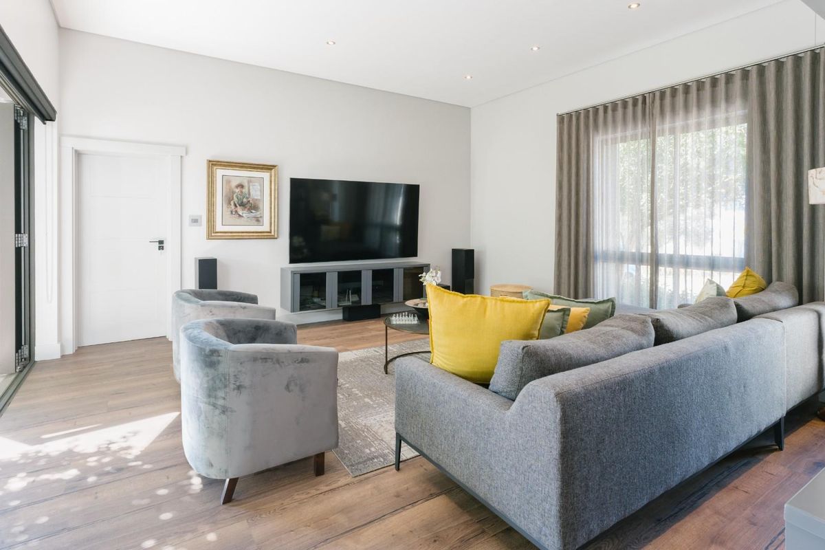 A bright and modern living room featuring timber flooring, recessed downlighting, and large sliding glass doors providing seamless access to the outdoor area.