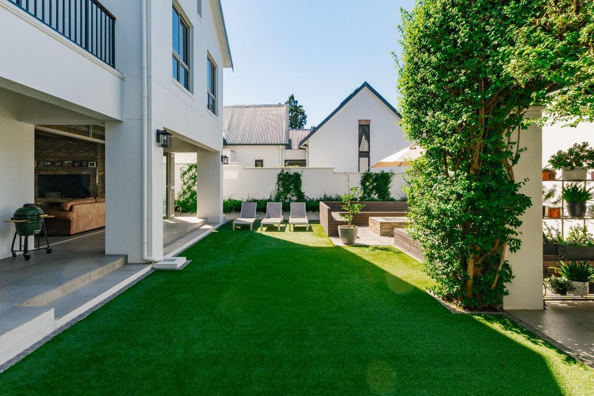A well-maintained rear garden featuring a manicured lawn, paved patio area, and seamless transition to the covered outdoor living space.