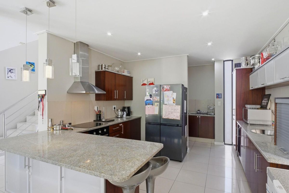 Modern kitchen featuring granite countertops, stainless steel appliances, ample cabinetry, and tiled flooring, seamlessly integrated with an open-plan living area and staircase.