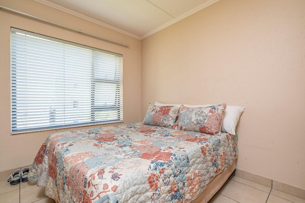 A functional bedroom featuring tiled flooring, a built-in wardrobe, and a window fitted with horizontal blinds.