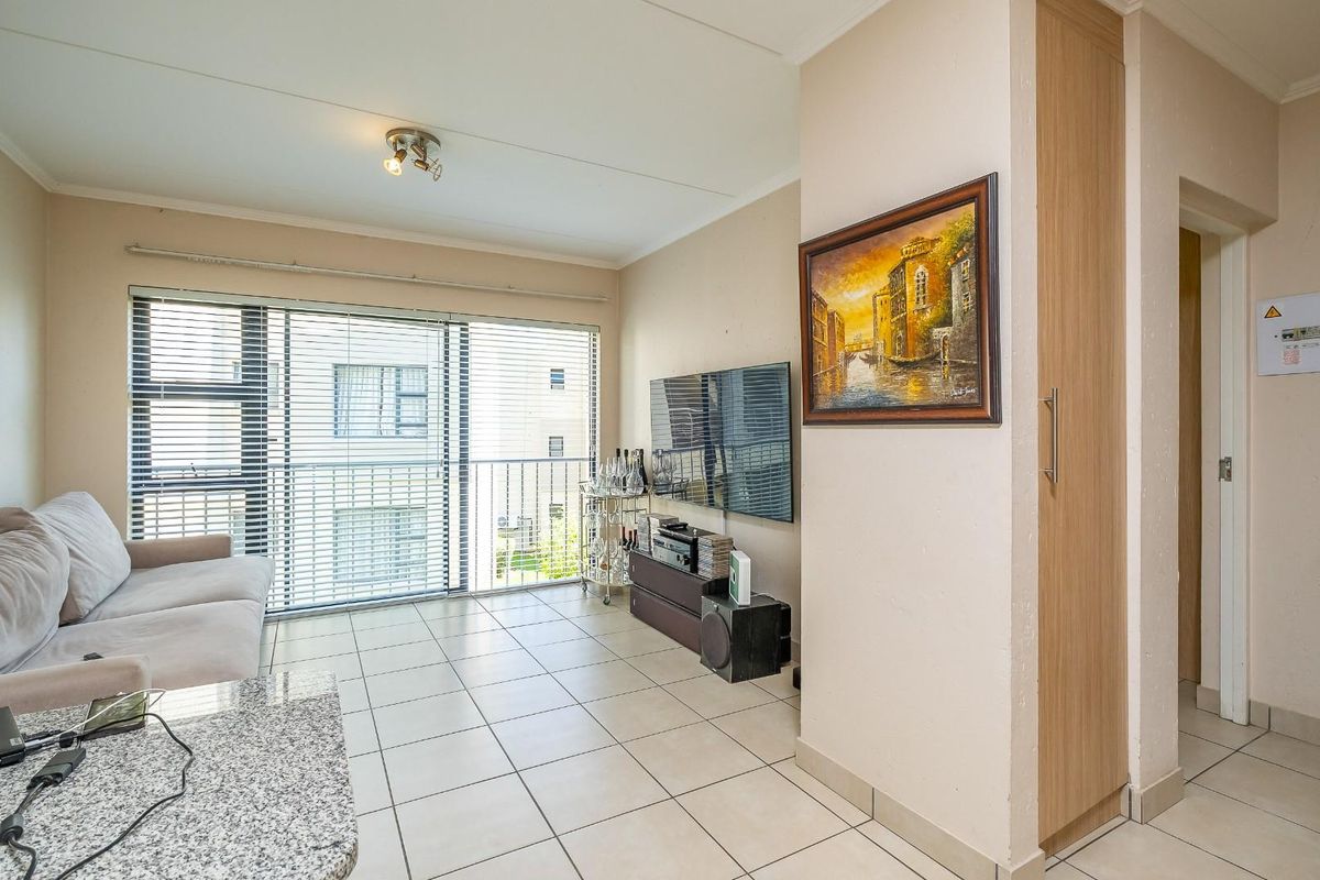 A bright living room featuring tiled flooring, a built-in storage cupboard, and large sliding glass doors leading to a balcony.