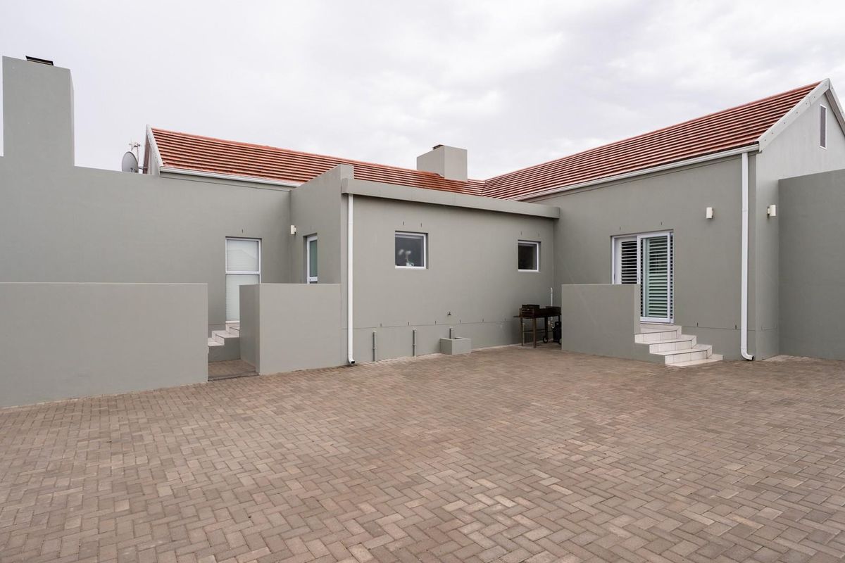 Rear view of the property featuring a paved courtyard, tiled roof, and multiple access points with steps.