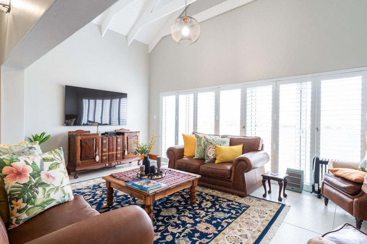 Spacious living room featuring high vaulted ceilings, exposed beams, and large folding glass doors with plantation shutters providing ample natural light.