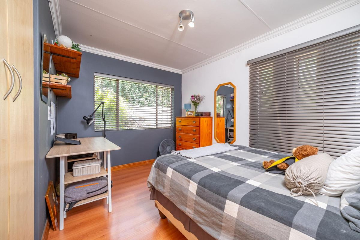 A well-lit bedroom featuring laminate flooring, horizontal window blinds, and a dark grey accent wall, providing a functional and comfortable living space.