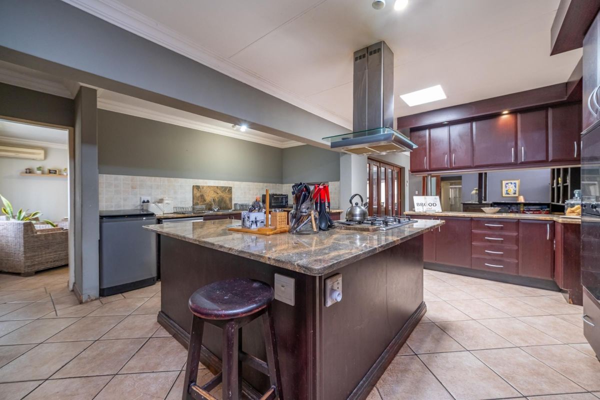 Spacious kitchen featuring a large central island with granite countertops, built-in gas hob, stainless steel extractor fan, and dark wood cabinetry.