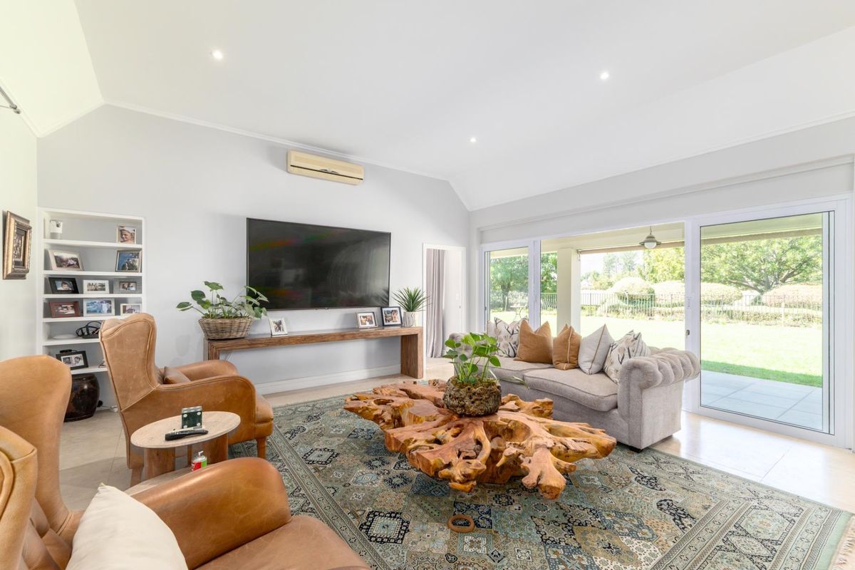 Spacious living room featuring high vaulted ceilings, recessed lighting, built-in shelving, and large sliding glass doors opening to a covered patio and garden.