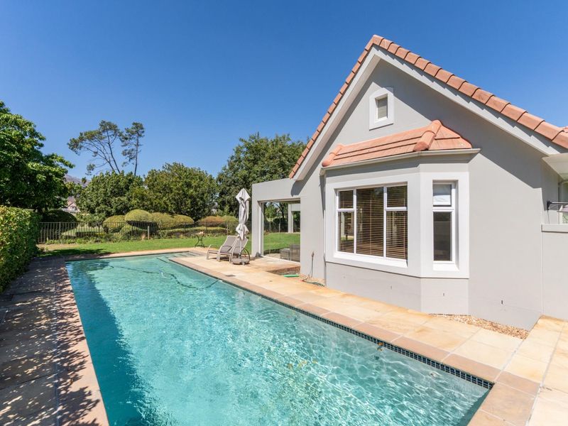 A well-maintained rear exterior view featuring a swimming pool, paved patio area, and landscaped garden with mature trees.