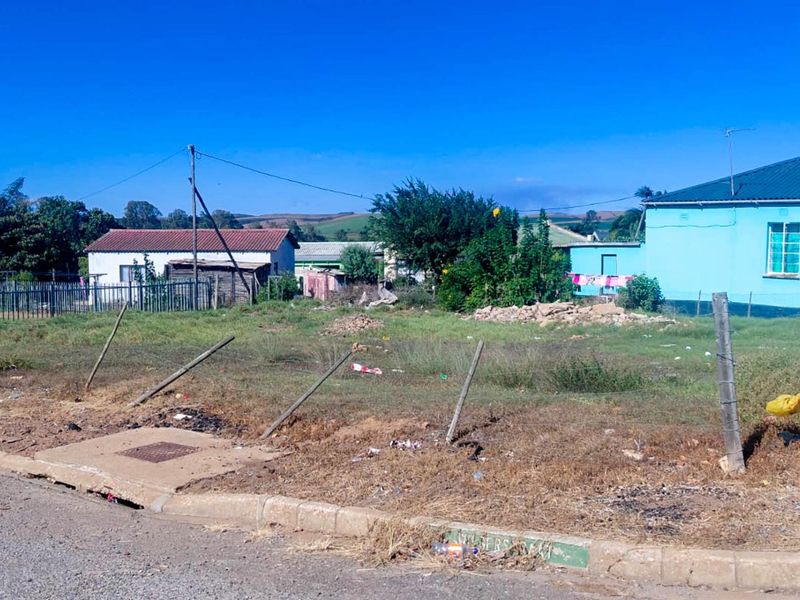 A vacant residential plot featuring a wire fence, concrete curb, and stormwater drain, situated in a neighborhood setting.