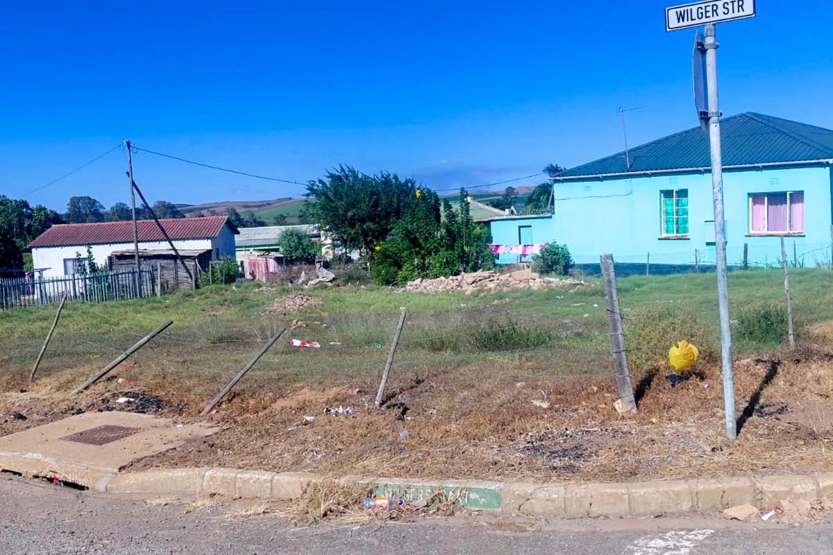 A vacant residential plot of land featuring a wire fence, concrete curb, and street signage, situated in a residential neighborhood.