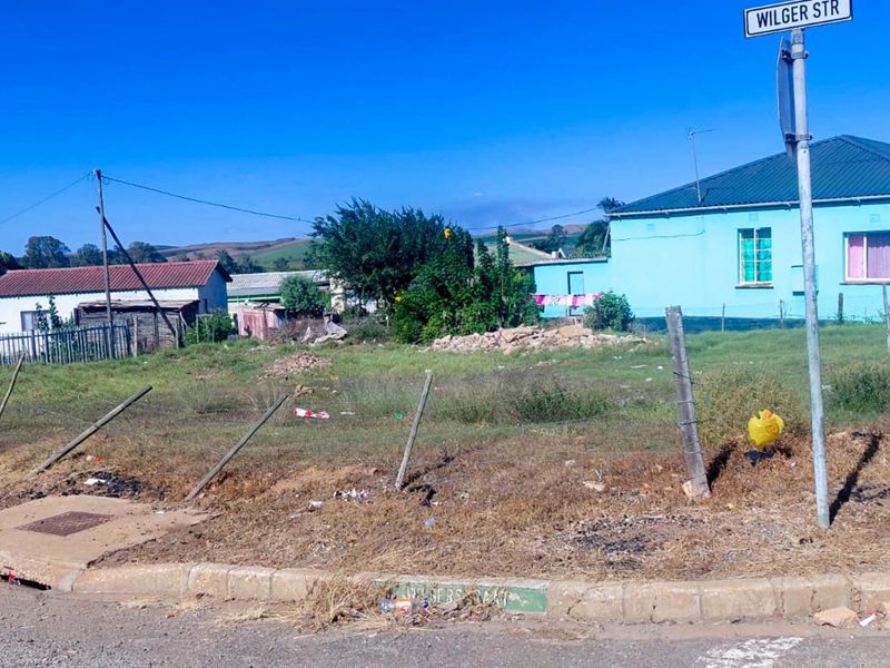 A vacant residential plot of land featuring a wire fence, concrete curb, and street signage, situated in a residential neighborhood.