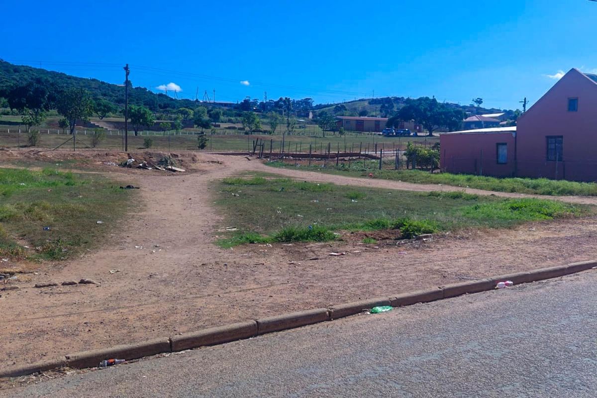 A street-level view of an unimproved residential vacant lot with a dirt access path and surrounding wire fencing.