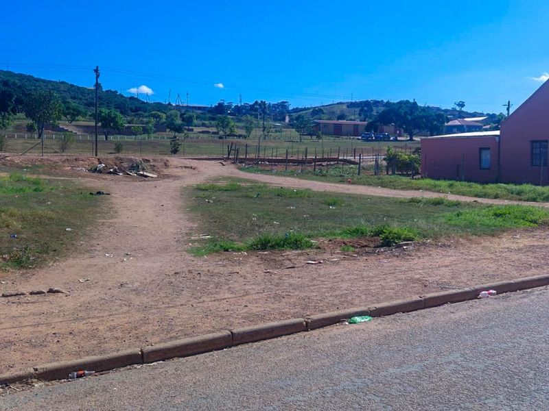 A street-level view of an unimproved residential vacant lot with a dirt access path and surrounding wire fencing.