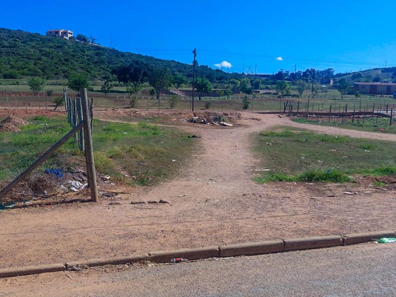 A vacant residential plot featuring natural terrain, wire fencing, and direct street access, offering a blank canvas for future development.