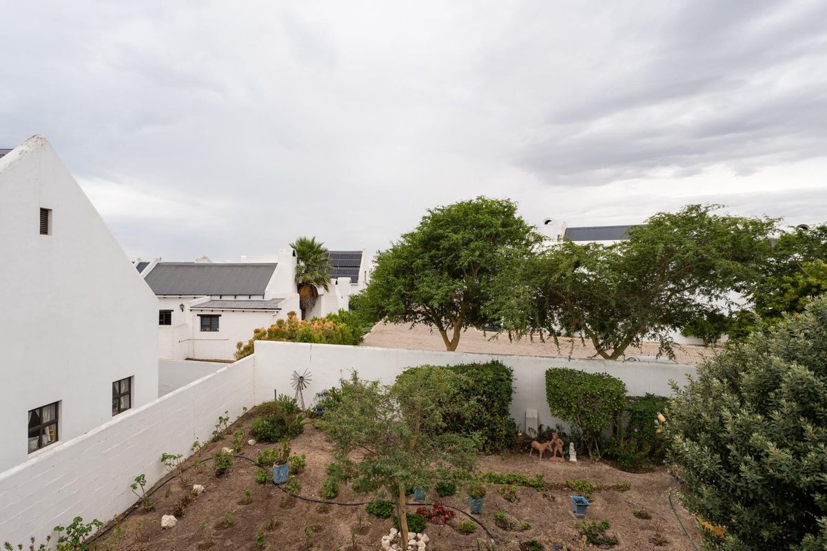 An elevated view of a rear garden area featuring a white boundary wall and surrounding residential architecture.