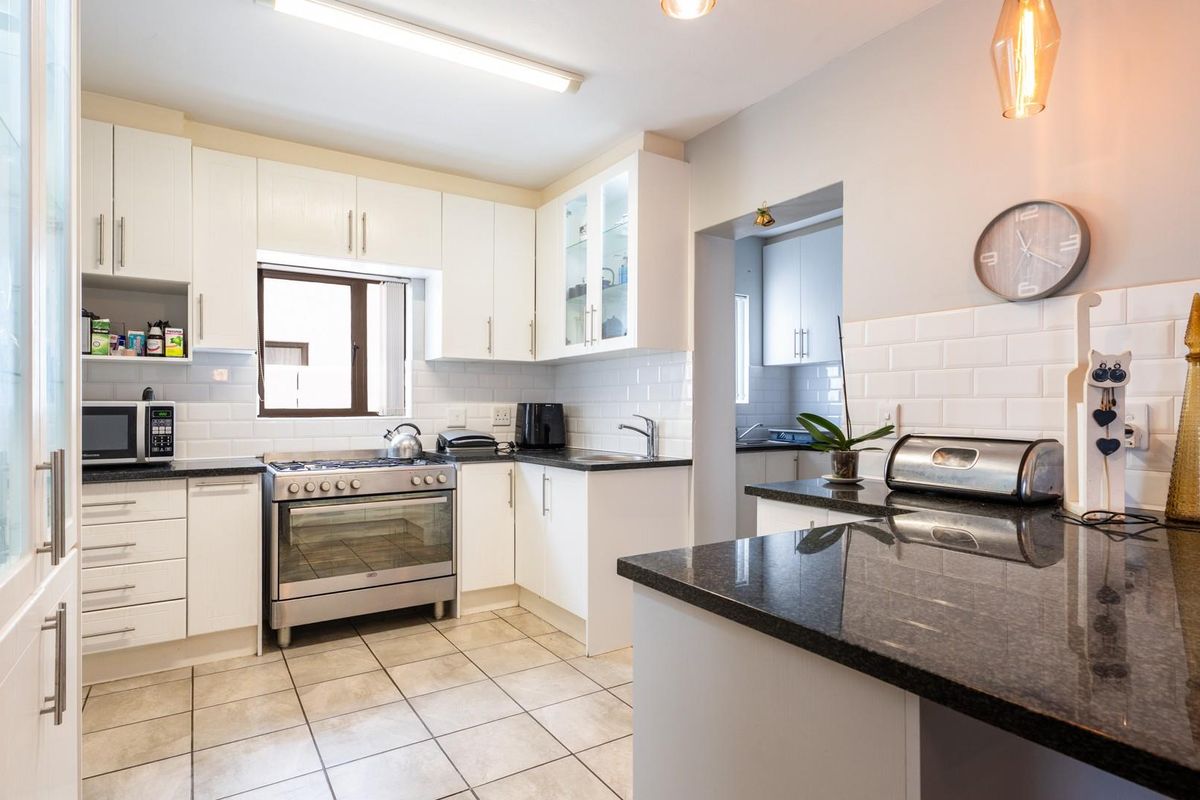 A well-maintained kitchen featuring white cabinetry, granite countertops, subway tile backsplash, and a freestanding gas stove, with an adjoining scullery area.