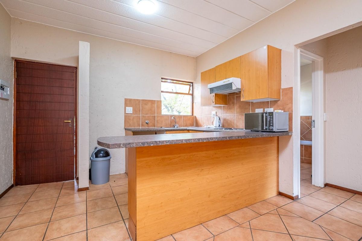 A functional kitchen featuring wooden cabinetry, a breakfast bar, tiled splashbacks, and tiled flooring, providing a practical layout for daily meal preparation.