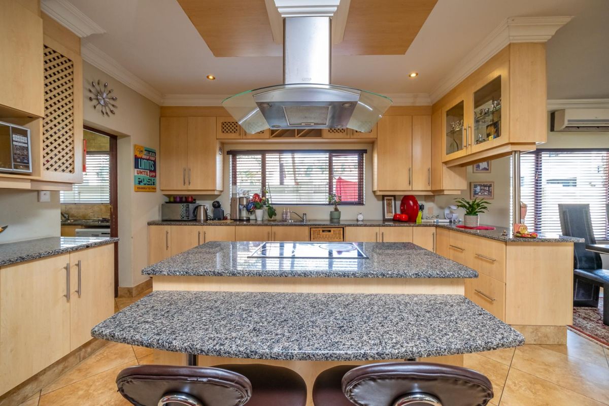 Spacious kitchen featuring light wood cabinetry, granite countertops, a central island with a built-in hob, and a stainless steel extractor fan.