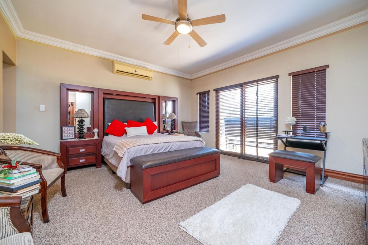 Spacious bedroom featuring a ceiling fan, wall-mounted air conditioning unit, and sliding glass doors with fitted blinds leading to an outdoor area.