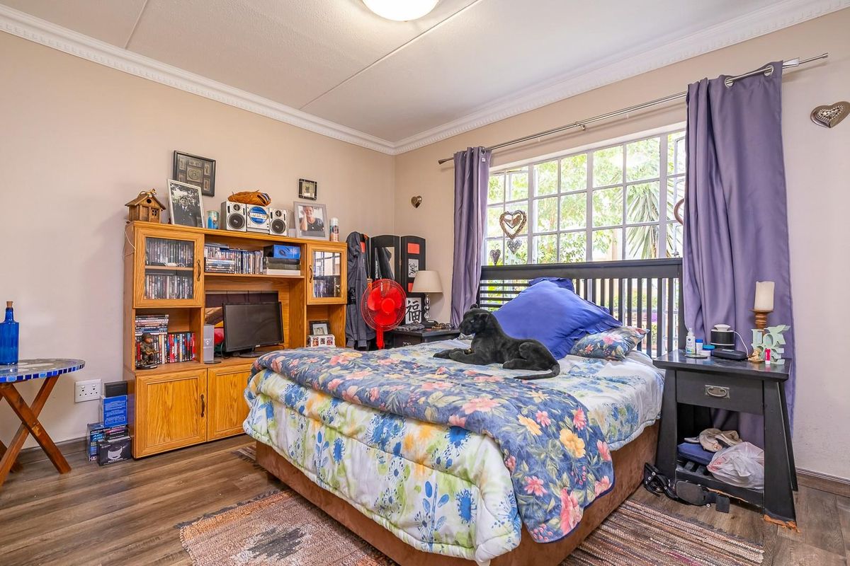 A bedroom featuring wood-look flooring, crown molding, and a large window with natural light.