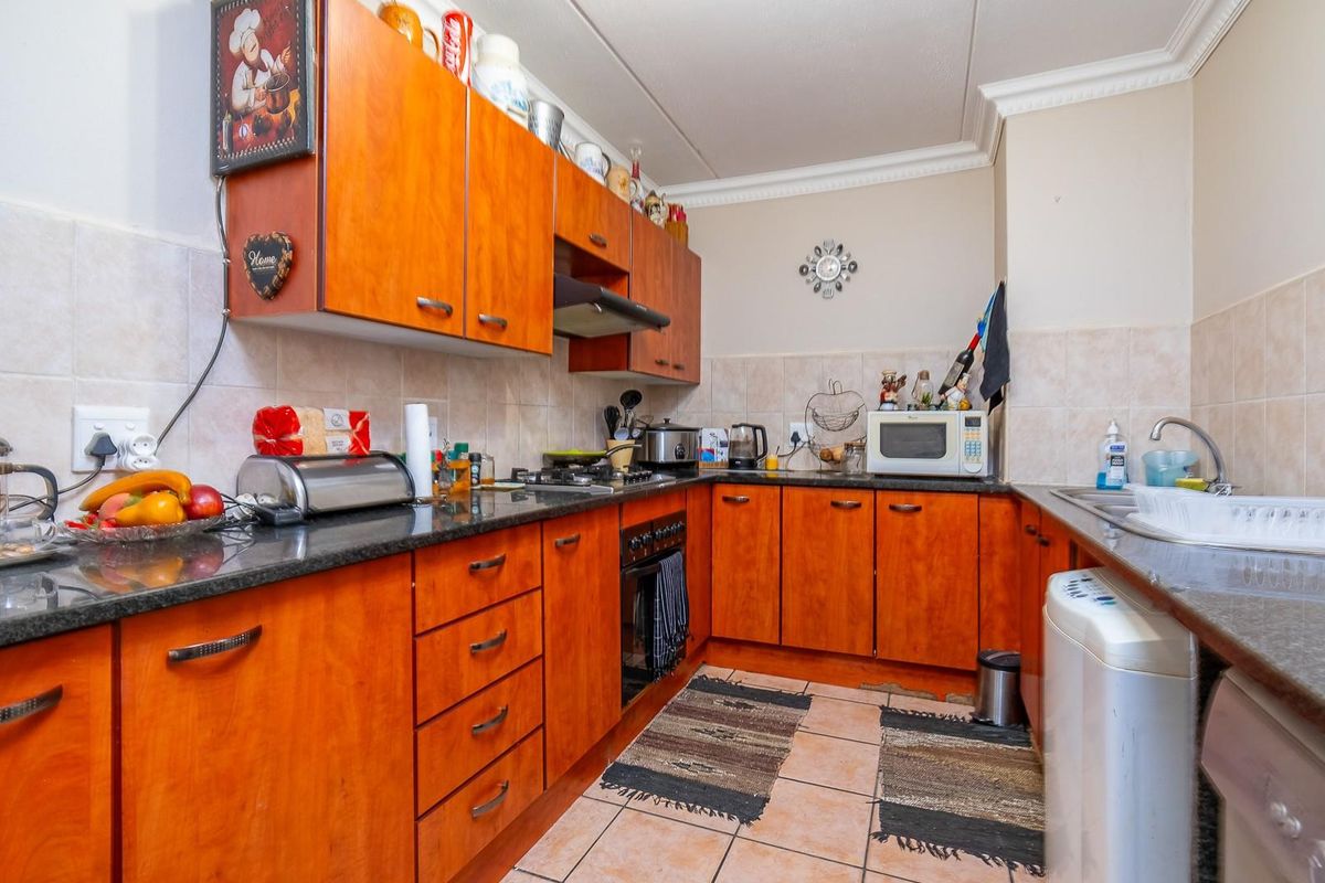 A functional kitchen featuring wooden cabinetry, granite countertops, tiled splashbacks, and integrated oven and extractor fan.
