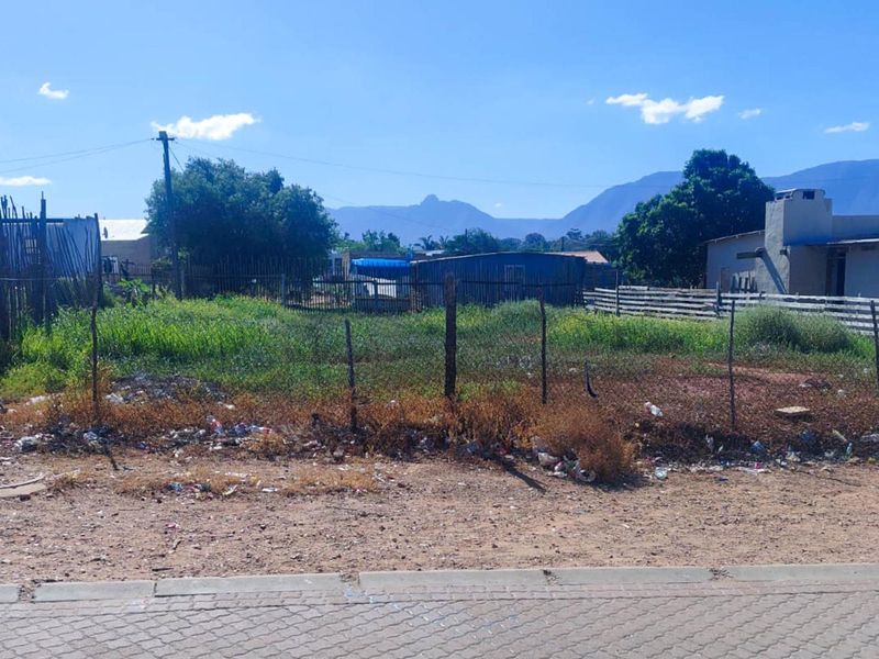 A vacant residential plot featuring a wire fence, utility pole, and mountain views, requiring clearing and site preparation.