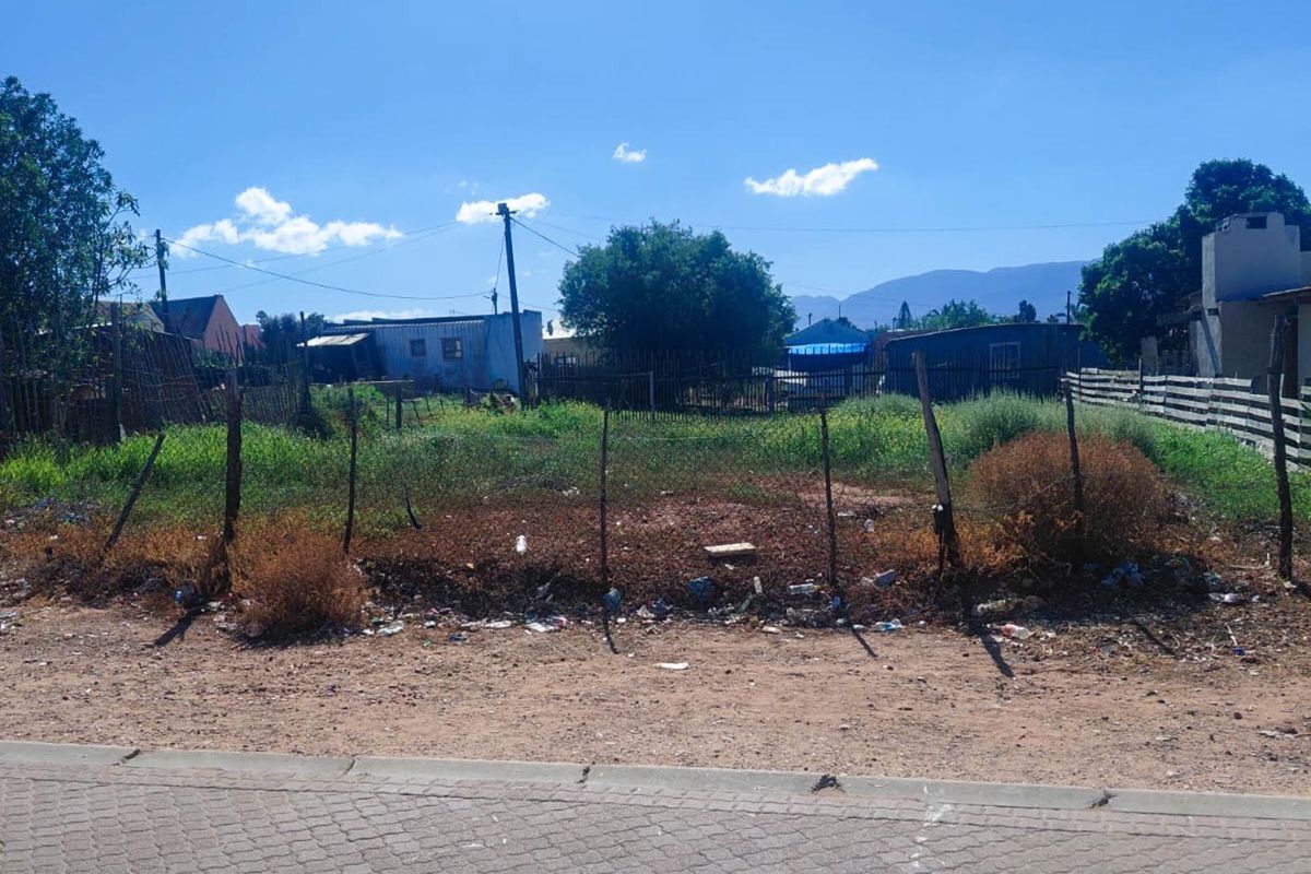 A vacant residential plot featuring wire fencing and a utility pole, situated in a neighborhood setting with mountain views in the distance.