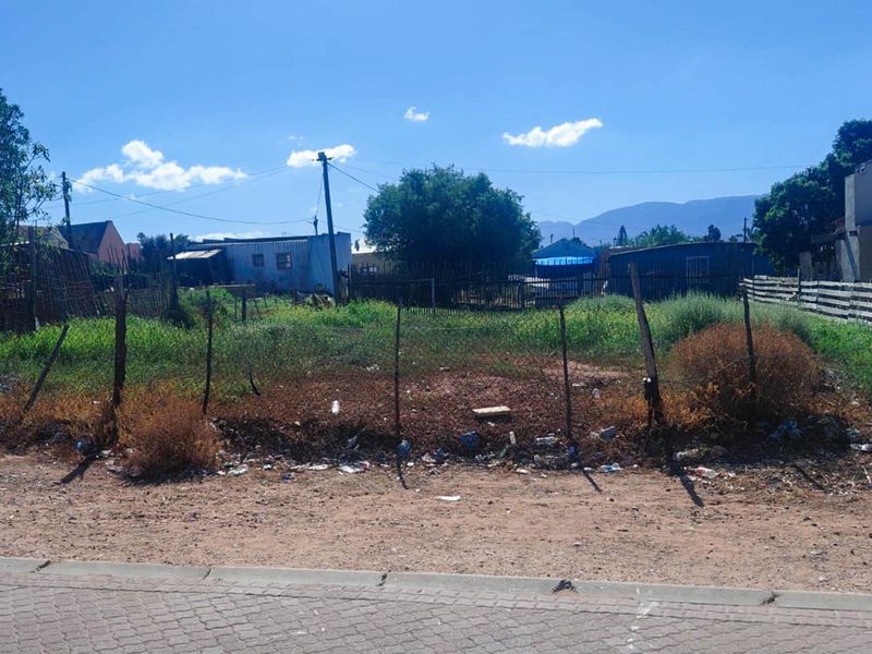 A vacant residential plot featuring wire fencing and a utility pole, situated in a neighborhood setting with mountain views in the distance.