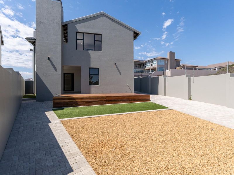 Rear view of the property featuring a modern grey facade, a raised timber deck, artificial lawn, and low-maintenance gravel landscaping.