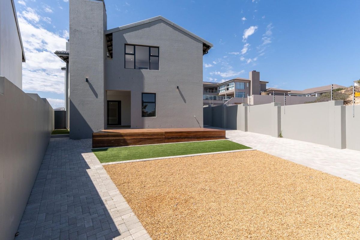 Rear view of the property featuring a modern grey facade, a raised timber deck, artificial lawn, and low-maintenance gravel landscaping.
