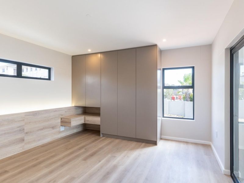 Modern bedroom featuring built-in cabinetry, integrated desk space, wood-look flooring, and large sliding glass doors leading to an outdoor area.