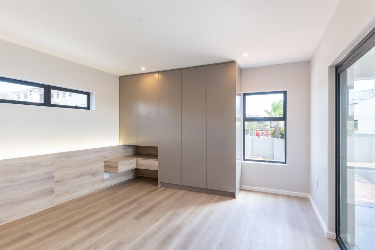 Modern bedroom featuring built-in cabinetry, integrated desk space, wood-look flooring, and large sliding glass doors leading to an outdoor area.