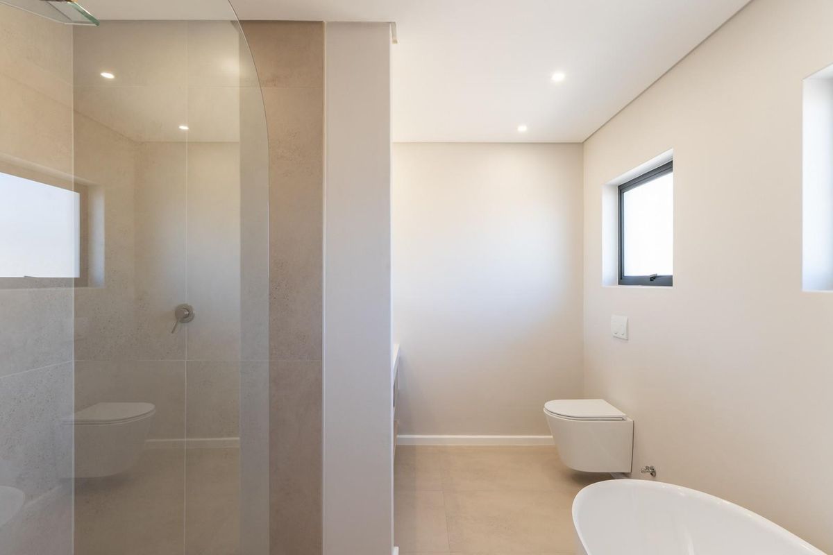 Modern bathroom featuring a glass-enclosed walk-in shower, wall-mounted toilet, and neutral floor-to-ceiling tiling with recessed lighting.